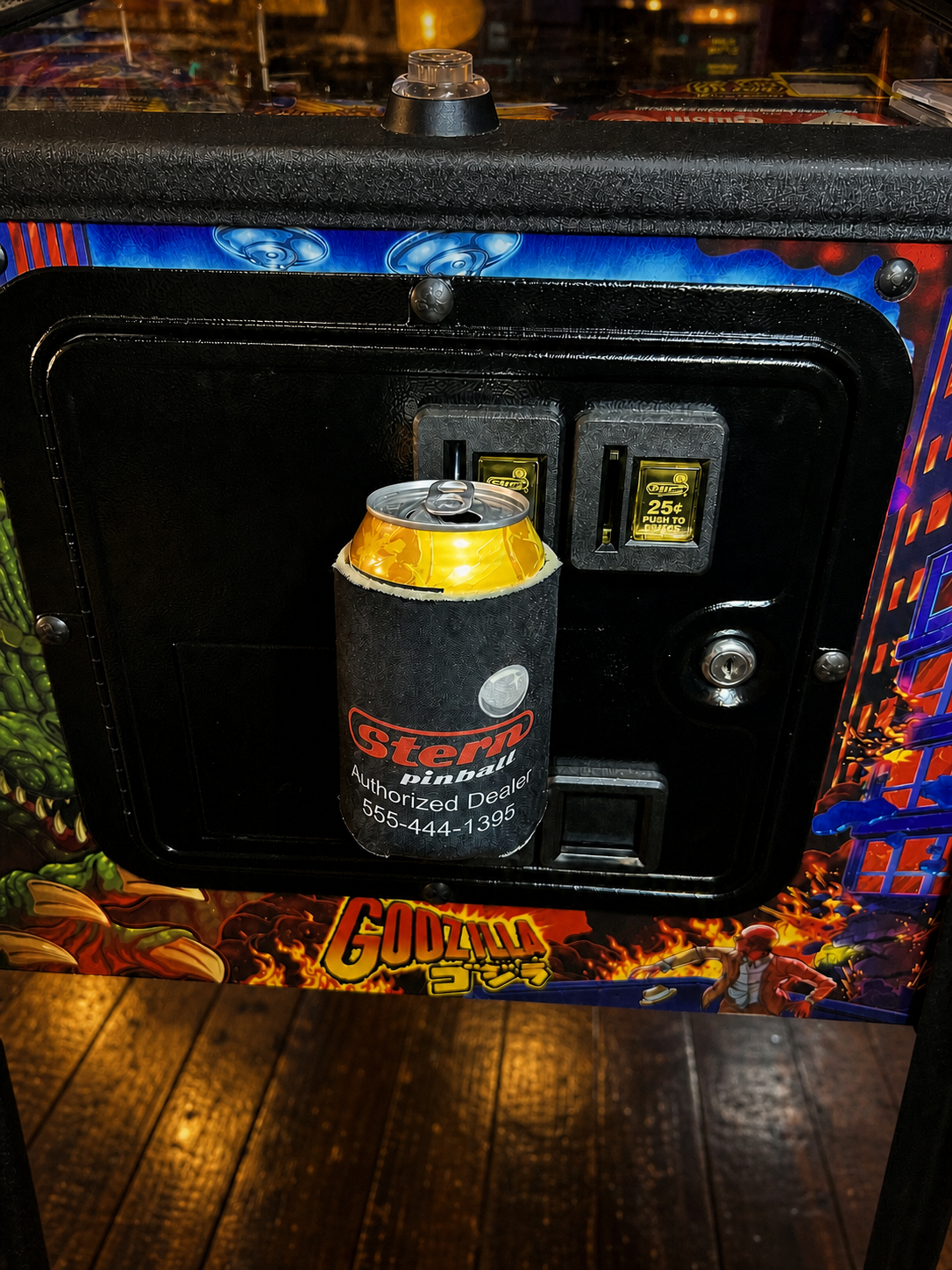 A drink in a koozie secured by a Coinzy Koozie Insert in a pinball machine coin slot.